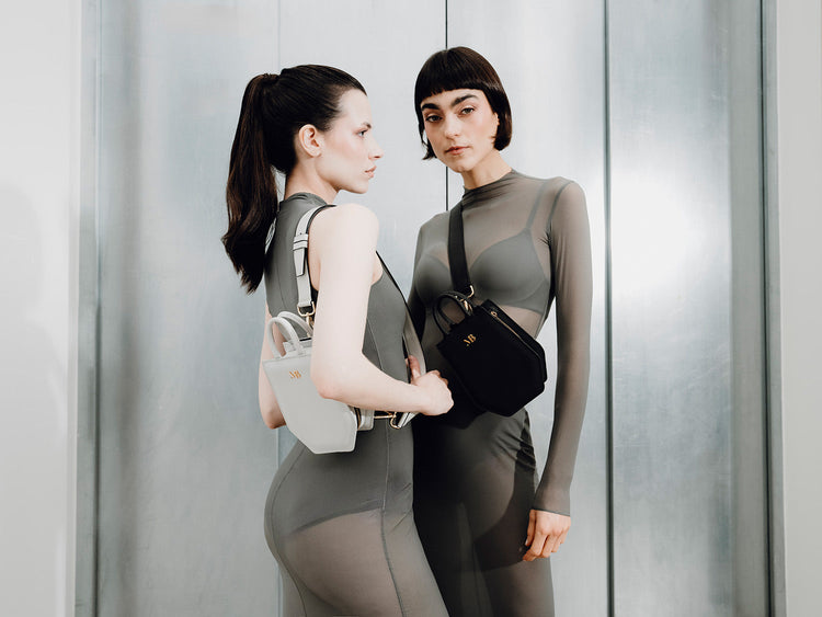 Model holding a brown vegan handbag by MELINA BUCHER, partially hidden behind a dark wall, wearing a cream blouse – minimalist and architectural aesthetic.